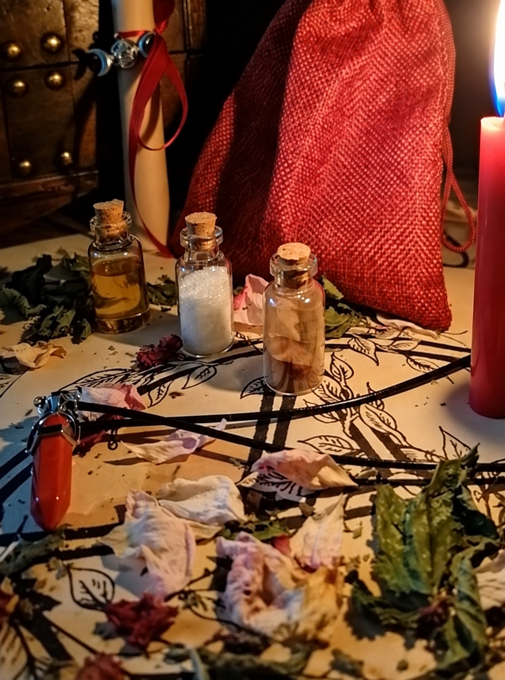 Illustrative close view of glass vials, dried plants and a pendant on the ritual cloth.