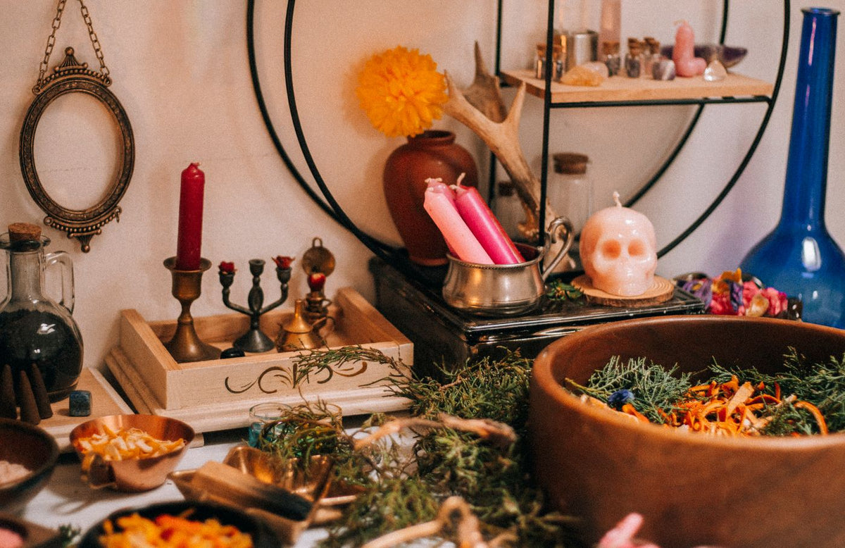 A personal witchcraft table with candles, herbs, botanical jars and ritual objects